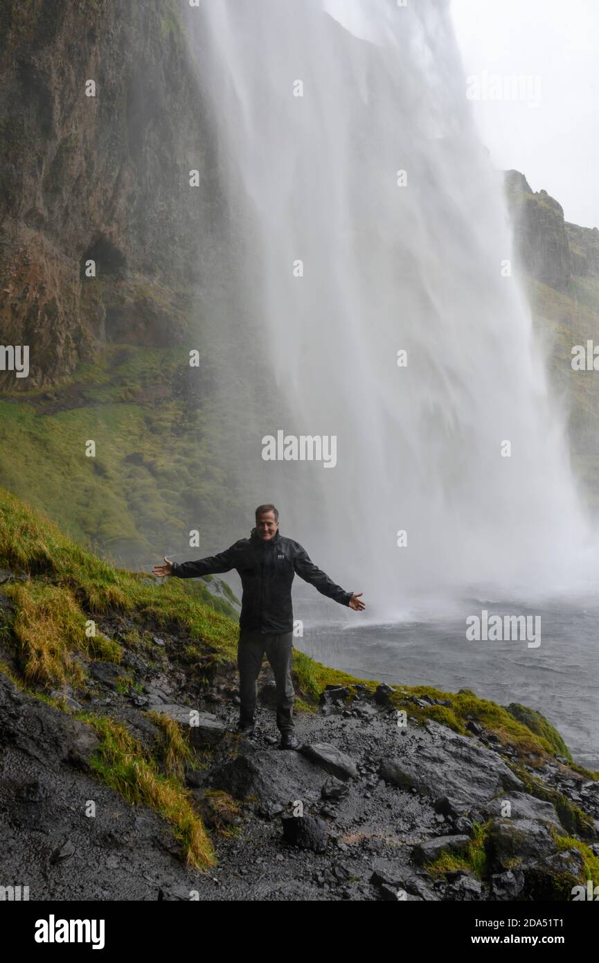 Mann, der vor einem Wasserfall steht, Seljalandsfoss, Rangarthing Eystra, Südliche Region, Island Stockfoto