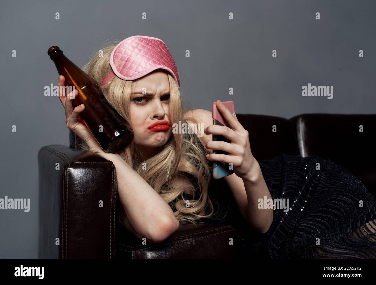 Eine Frau in einer rosa Maske liegt auf der Couch Mit einer Flasche Bier und einem Telefon in ihr Hand Stockfoto