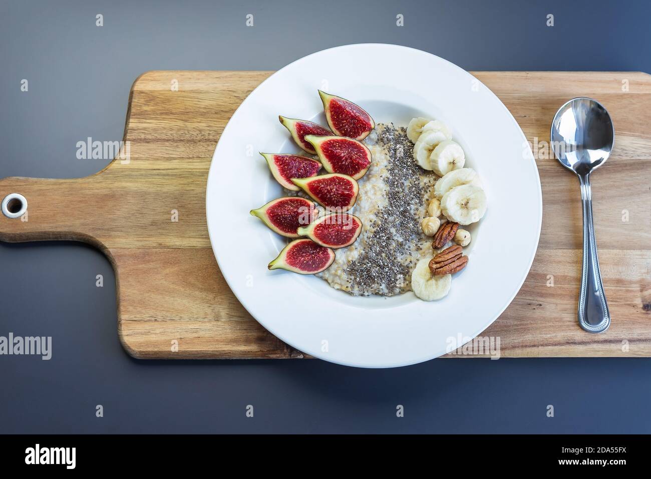 Eine Schüssel mit Frühstück Haferbrei Haferbrei mit Superfood Chia Samen, frische Feigen und Banane auf einem Holzbrett auf grauem Hintergrund , serviert mit schwarzem Tee Stockfoto