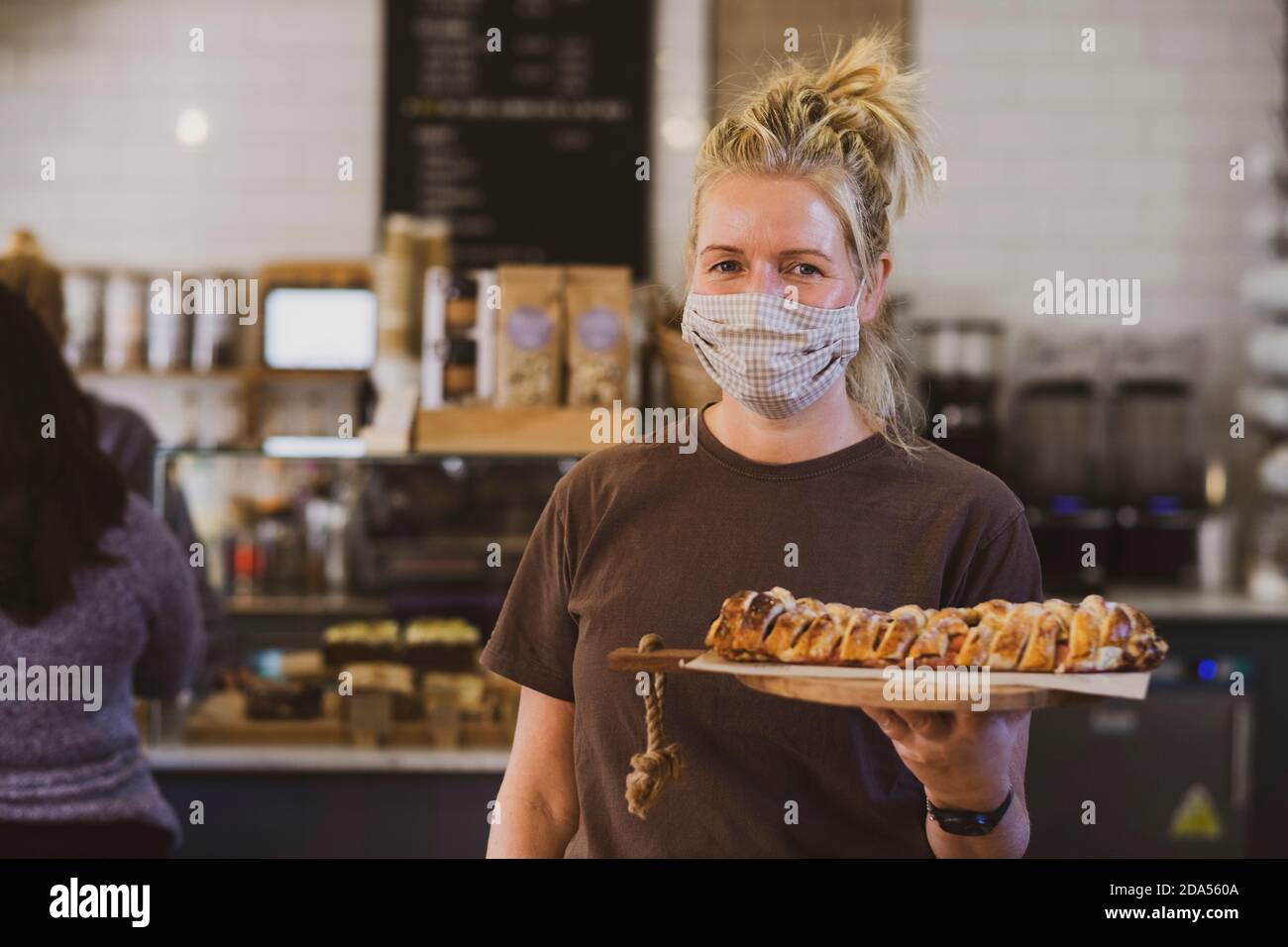 Blonde Kellnerin trägt Gesichtsmaske in einem Café arbeiten, tragen Teller mit Lebensmitteln. Stockfoto