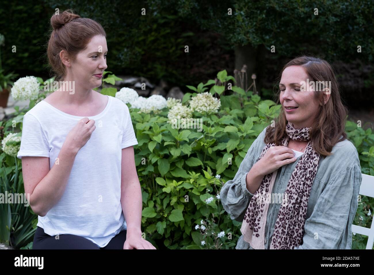 Therapeut und Klientin sitzen in einem Garten, Frauen mit Händen auf dem Brustbein Stockfoto