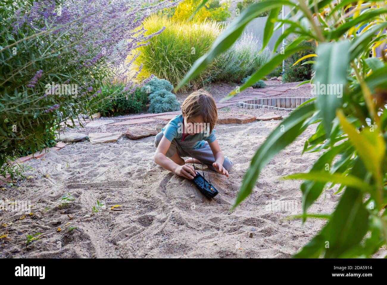 7 Jahre alter Junge spielt im Sandgarten mit seinem Spielzeugschiff. Stockfoto