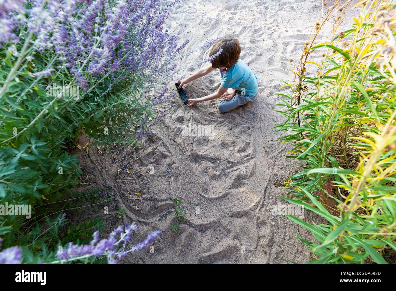 7 Jahre alter Junge spielt im Sandgarten mit seinem Spielzeugschiff. Stockfoto