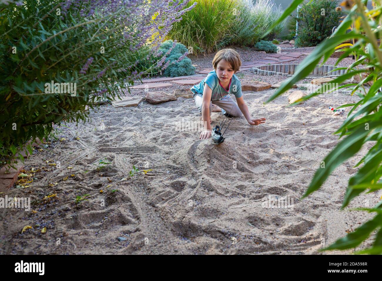 7 Jahre alter Junge spielt im Sandgarten mit seinem Spielzeugschiff. Stockfoto