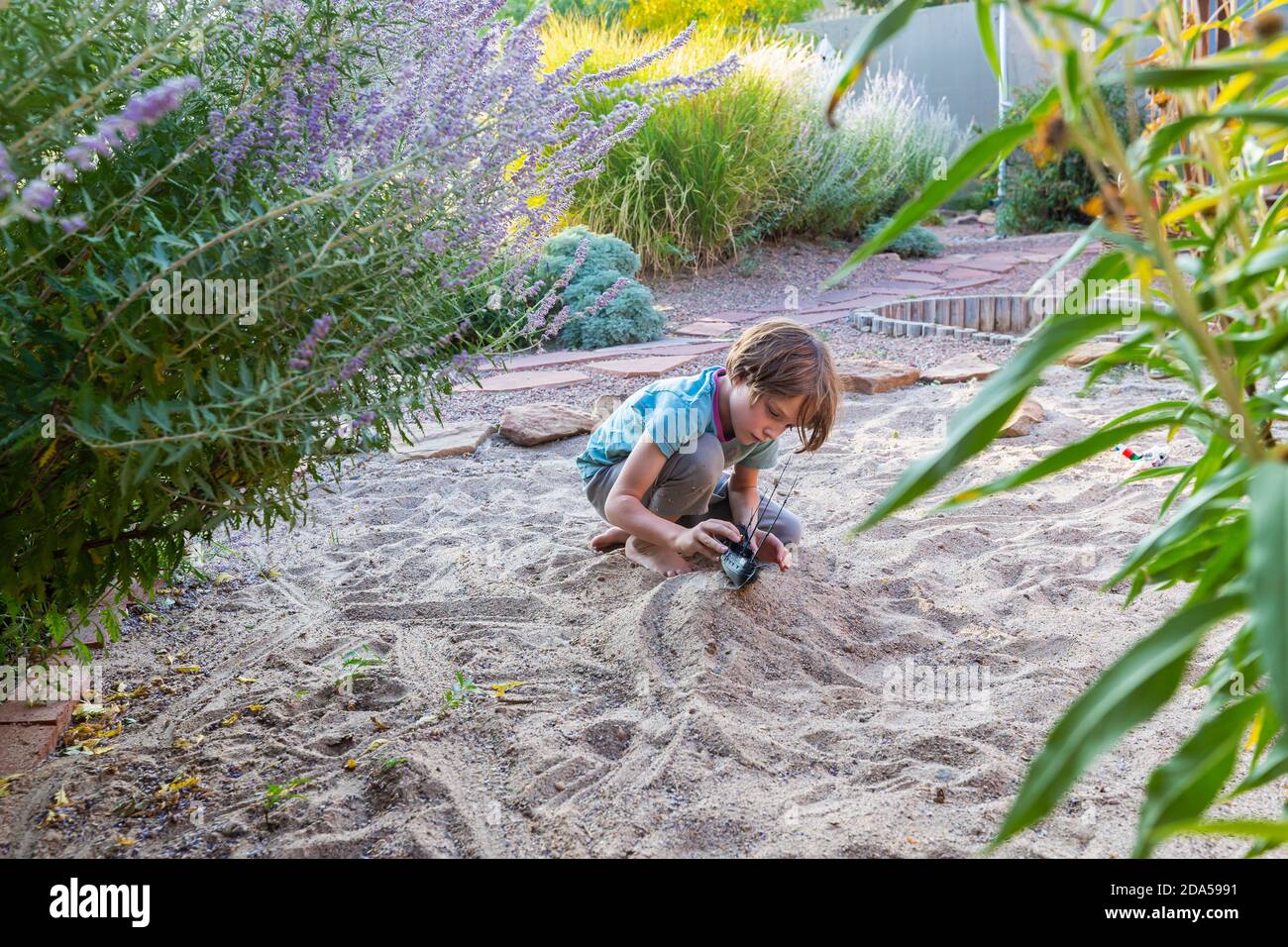 7 Jahre alter Junge spielt im Sandgarten mit seinem Spielzeugschiff. Stockfoto