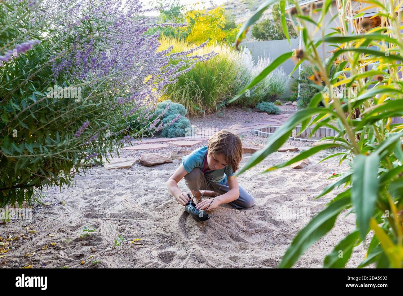 7 Jahre alter Junge spielt im Sandgarten mit seinem Spielzeugschiff. Stockfoto