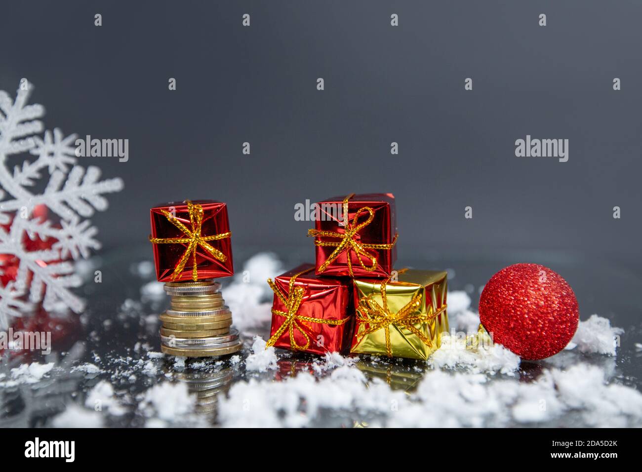 Münzen, weihnachtskugel, kleine Geschenke auf grauem verschwommenem Hintergrund, weihnachtsdekoration Stockfoto