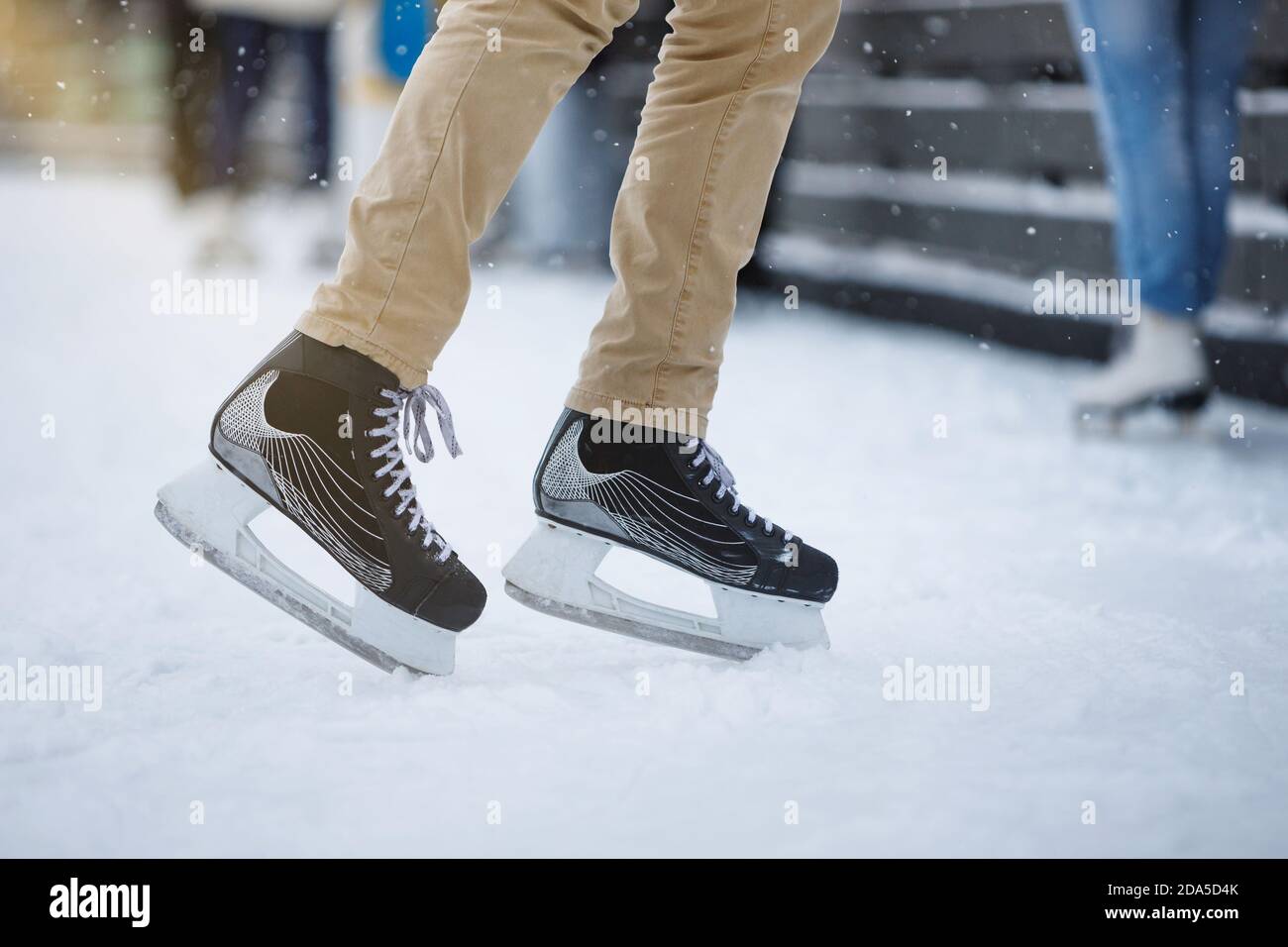 Nahaufnahme der Beine des Eislaufes auf der Außeneisbahn, Ansicht von unten. Männer stehen und posiert in schwarzen Schlittschuhe auf weißem Eis Stockfoto