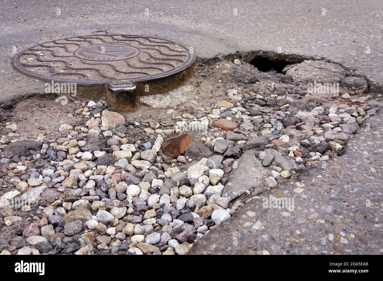 Zerstörte Asphaltstraße, Loch neben Sanitärinstallschacht Stockfoto