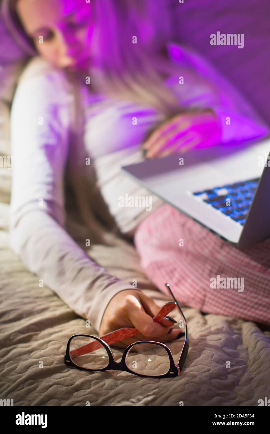 Verschwommene junge kaukasische Frau mit Brille in der Hand halten, schlafen nach der Arbeit spät in der Nacht auf Laptop-Computer, konzentrieren sich auf Brille. Schlaf, overt Stockfoto