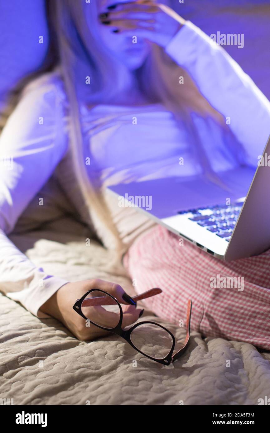 Verschwommene junge Frau mit Brille in der Hand halten, schlafen nach der Arbeit spät in der Nacht auf ihrem Laptop-Computer, konzentrieren sich auf Brille. Schlaf, Überstunden AA Stockfoto