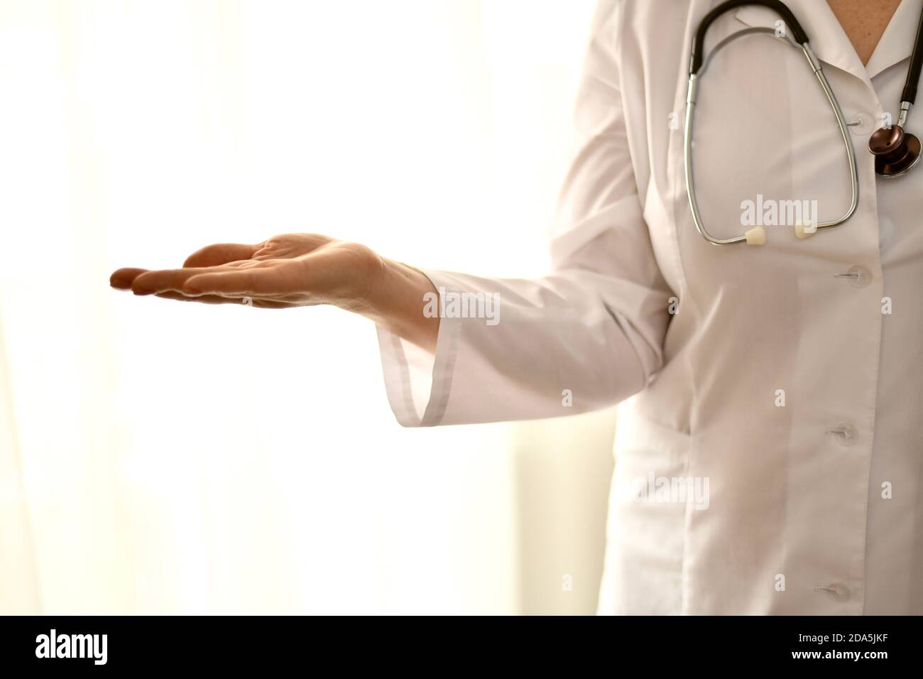 Der Arzt in einer weißen Robe steht, Nahaufnahme, die linke Seite der Person auf der rechten Seite, mit leerer Handfläche, die alles zeigt. Stockfoto