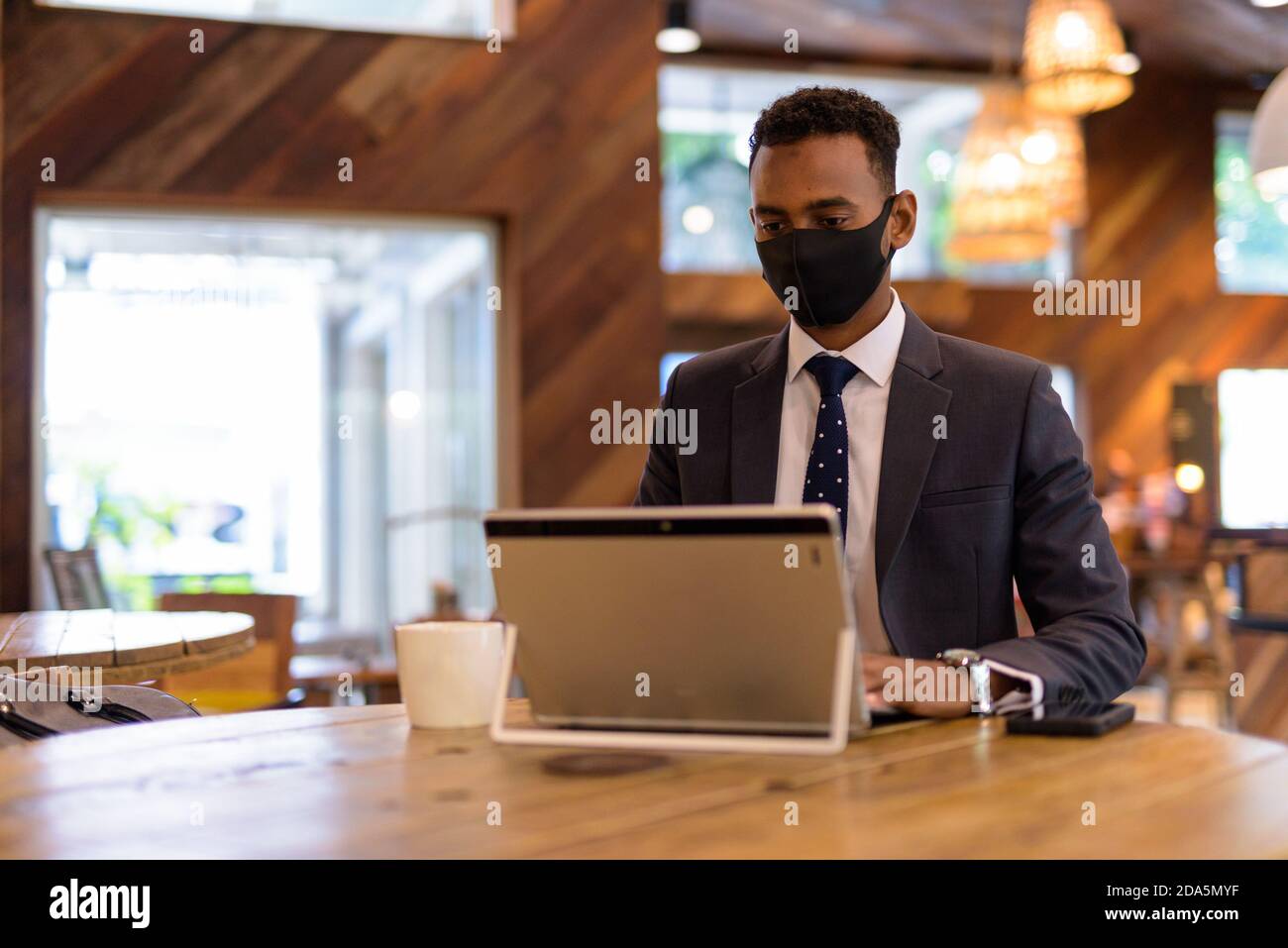 Geschäftsmann mit Laptop, während das Tragen einer schützenden Gesichtsmaske im Kaffee Kaufen Stockfoto