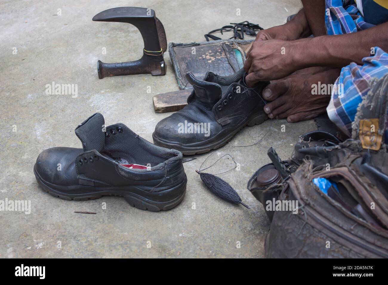 Indische lokale Schuster Reparatur Schuhe neben der Straße von Hand mit Werkzeugen in traditioneller Weise. Natürliche Schuss Darstellung der täglichen Arbeit eines regelmäßigen Schuster. Stockfoto