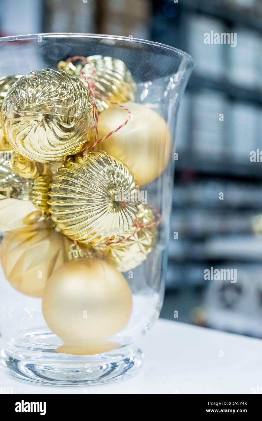 Weihnachtsschmuck in Glasvase auf Stoff Hintergrund.Weihnachtsbaum Spielzeug in große Vase. Goldene Glanzkugeln. Heimtextilien.Neujahr Ornamente Stockfoto