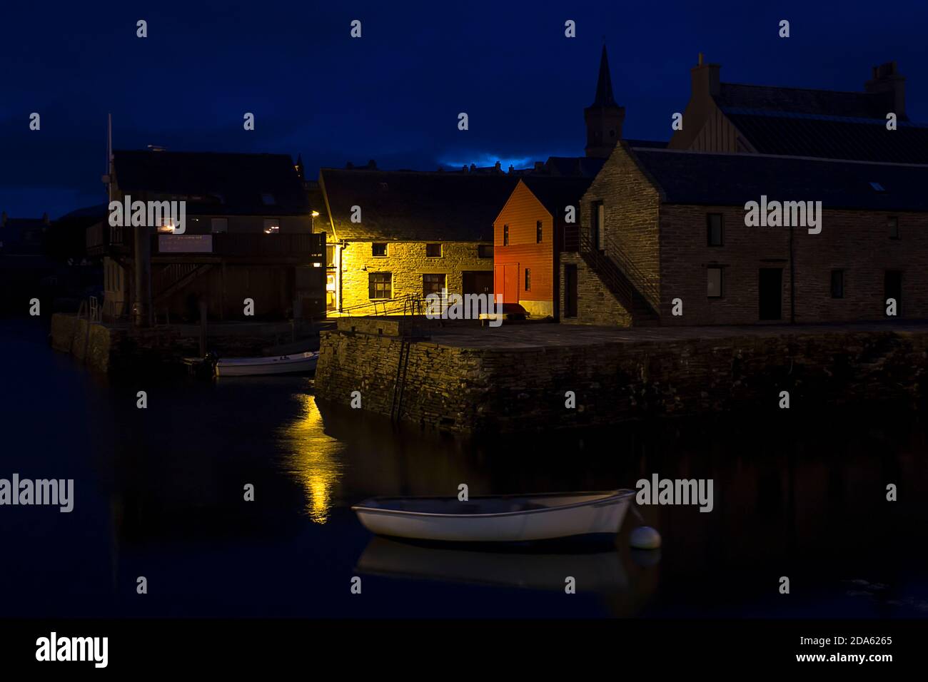 Blaue ruhige Nacht in Orkney Hafen mit Gebäuden und weiß Boot Stockfoto