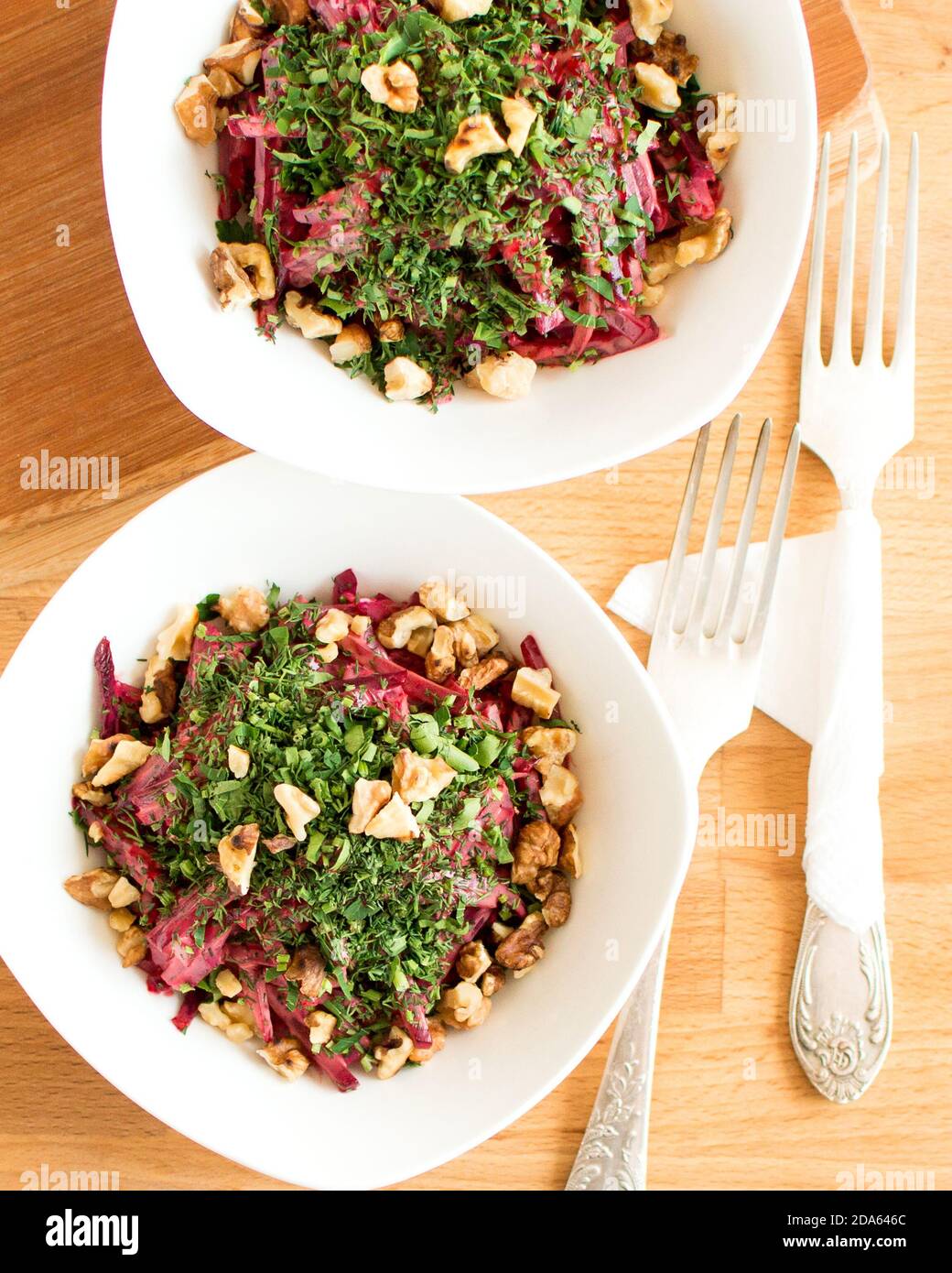 Salat mit gekochten Rüben und Walnüssen. Zwei Portionen in einer weißen Platte. Die Gabeln liegen nebeneinander. Stockfoto