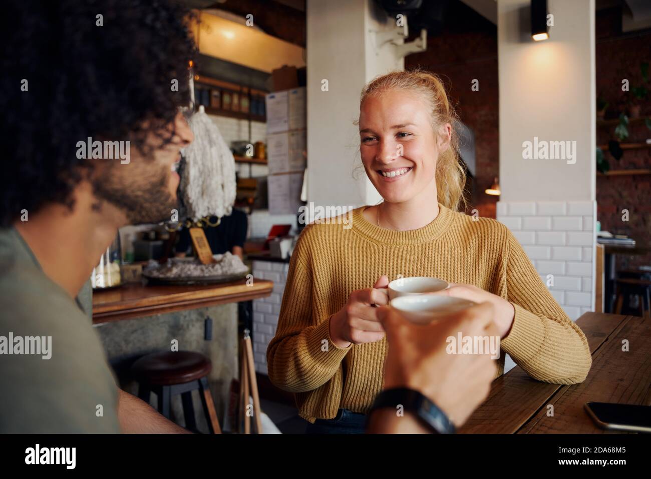 Portrait der schönen jungen Frau hält Kaffeebecher und reden Mann mit lockigen Haaren in einem modernen Café Stockfoto