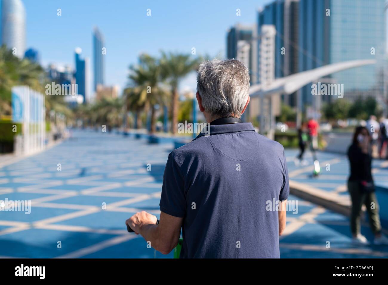 Senior Mann mit einer Fahrt auf Elektroroller für den Transport In einer modernen Stadtumgebung Rückansicht Stockfoto