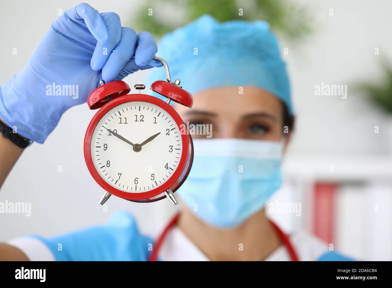 Arzt in der medizinischen Schutzmaske hält roten Wecker in Seine Hände Stockfoto