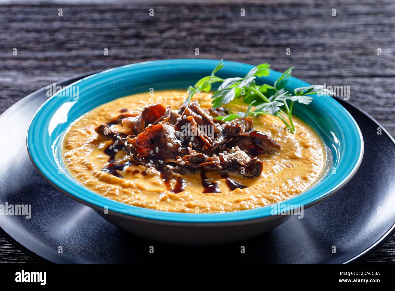 Kürbissuppe aus geröstetem Kürbispüree und Wildpilzbrühe, garniert mit Sesam, veganes Gemüsegericht, serviert auf einem blauen Teller mit Löffel und Ga Stockfoto