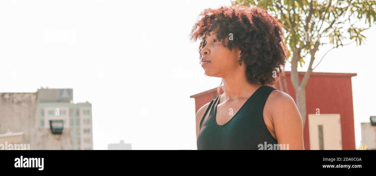 Junge afroamerikanische Frau, die weit entfernt in die Skyline von Gebäuden auf Dächern schaut. Weibliche Athlete bestimmt im Sport-Outfit mit Kopieplatz Stockfoto