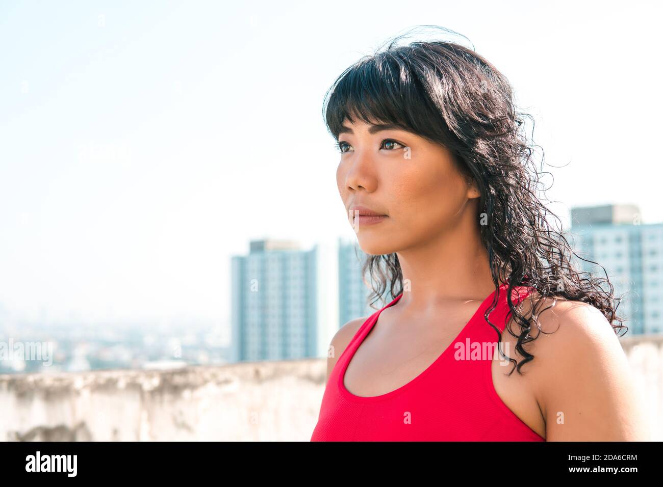 Junge asiatische Frau, die weit entfernt in die Skyline von Gebäuden auf Dächern schaut. Weibliche Athlete bestimmt im Sport-Outfit mit Kopieplatz Stockfoto