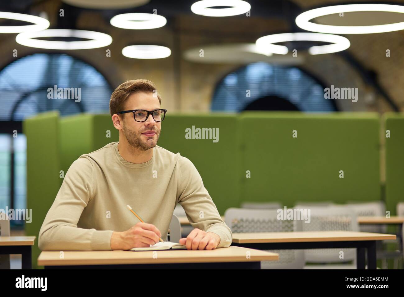 Kaukasischer Mann, männlicher Büroangestellter, der am Schreibtisch im Coworking Space sitzt und sich während des Corporate Trainings oder Seminars Notizen macht. Business Education Konzept Stockfoto