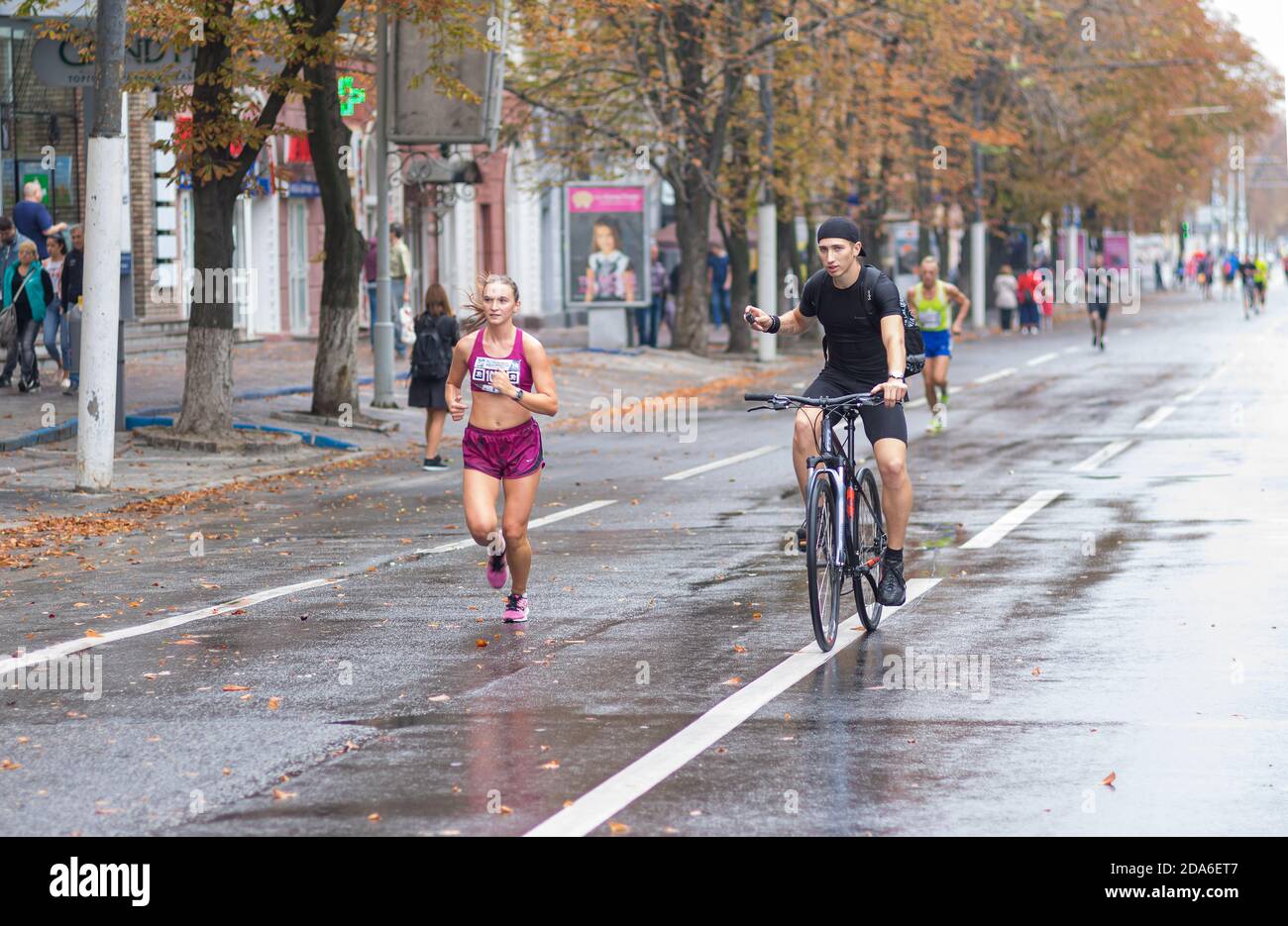 DNIPRO, UKRAINE - 16. SEPTEMBER 2018: Junger Mann auf einem Fahrrad Drehvideo der jungen Frau läuft während 21 km Entfernung von ATB Dnipro Marathon auf r Stockfoto