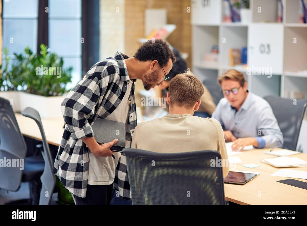 Rückansicht von zwei jungen Kollegen, die im modernen Büro oder Coworking Space gemeinsam etwas diskutieren. Konzept für Teamarbeit und Zusammenarbeit Stockfoto