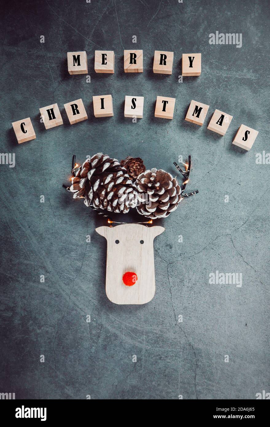 Fröhliches Weihnachts-Poster mit Holzregenhirsch, roter Nase, Kiefern und Weihnachtslichtern auf grauem Hintergrund. Weihnachtsstimmung. Weihnachtskarte. Stockfoto