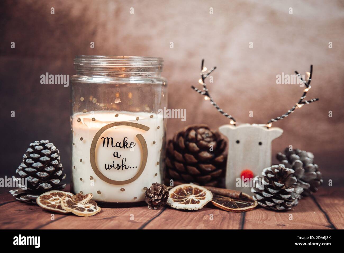 Weihnachtskomposition mit "Make a wish" Kerze in einem Glas mit Regenhirsch, Weihnachtsbeleuchtung und Tannenzapfen auf einem rustikalen braunen Hintergrund. Weihnachten Stockfoto