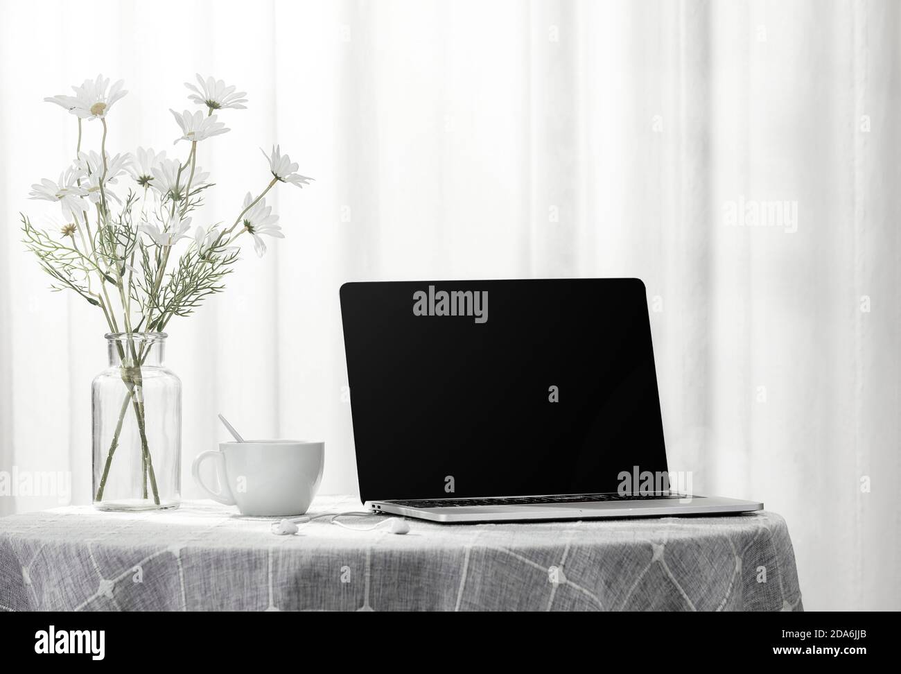 Laptop und eine Tasse Kaffee neben einer Vase voller Blumen, drinnen Stockfoto