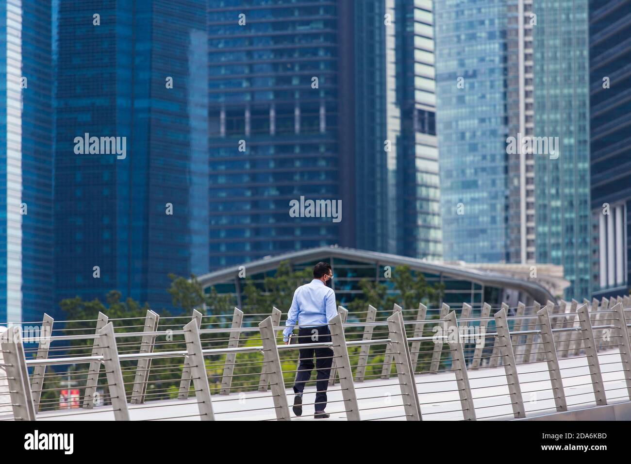 Die ganze Rückenansicht des Büroangestellten trägt eine schwarze Maske und läuft auf der Brücke in einer Geschäftsvierteln-Stadt, Singapur. Stockfoto