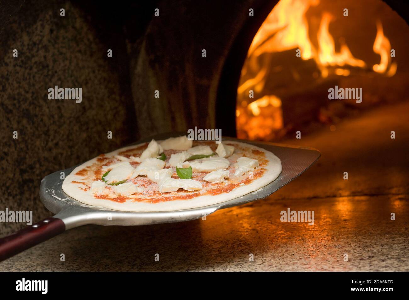 Der Pizzabäcker backt eine echte margherita Pizza im Holzofen mit der Schaufel Stockfoto