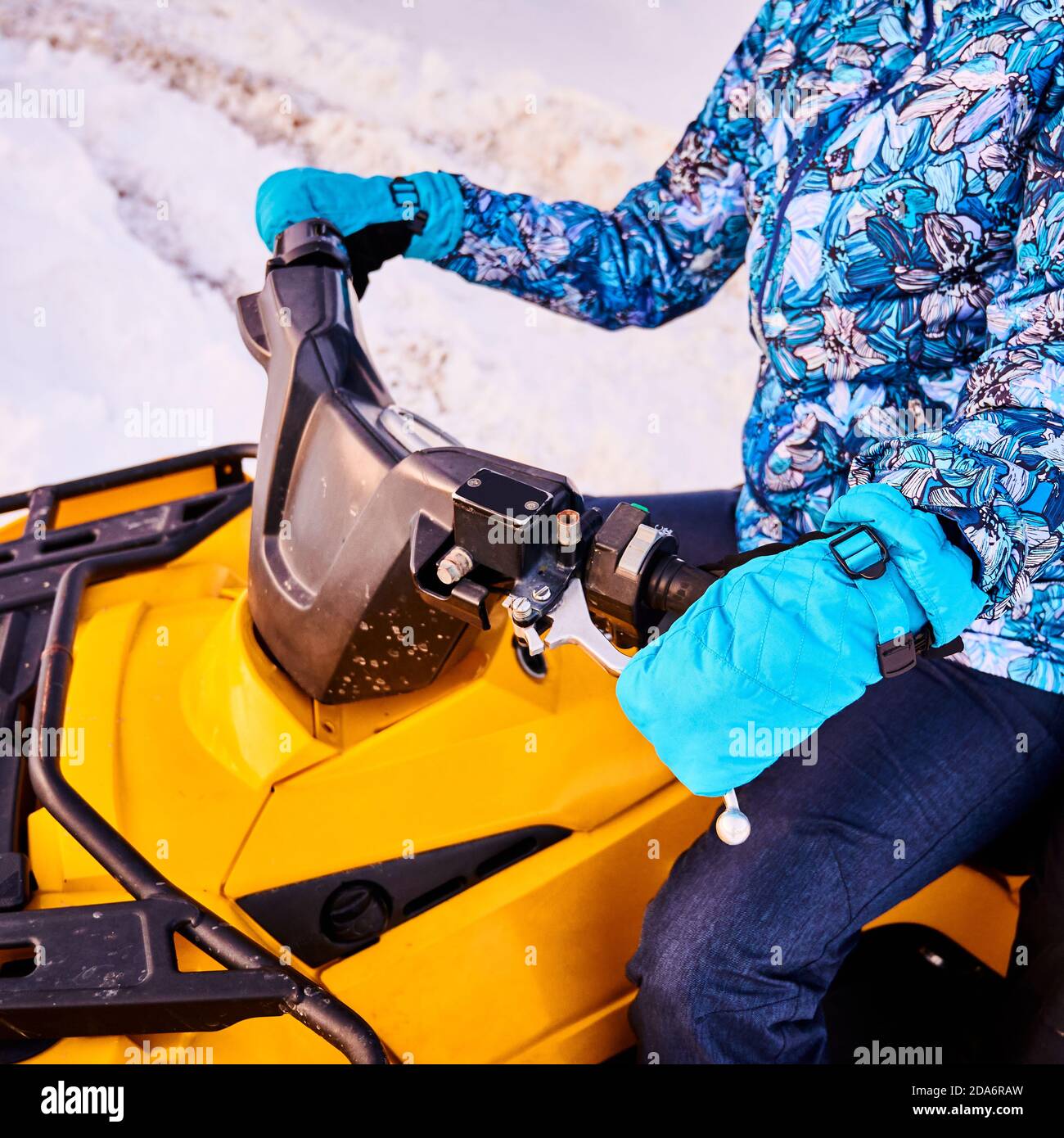 Beschnittene Nahaufnahme der Person in blauem Winteranzug und Fäustlingen, sitzend auf gelbem ATV-Fahrrad, das im Winter das Ruder hält, diagonaler Schnappschuss. Konzept des Wintersports und Quad-Biking. Stockfoto