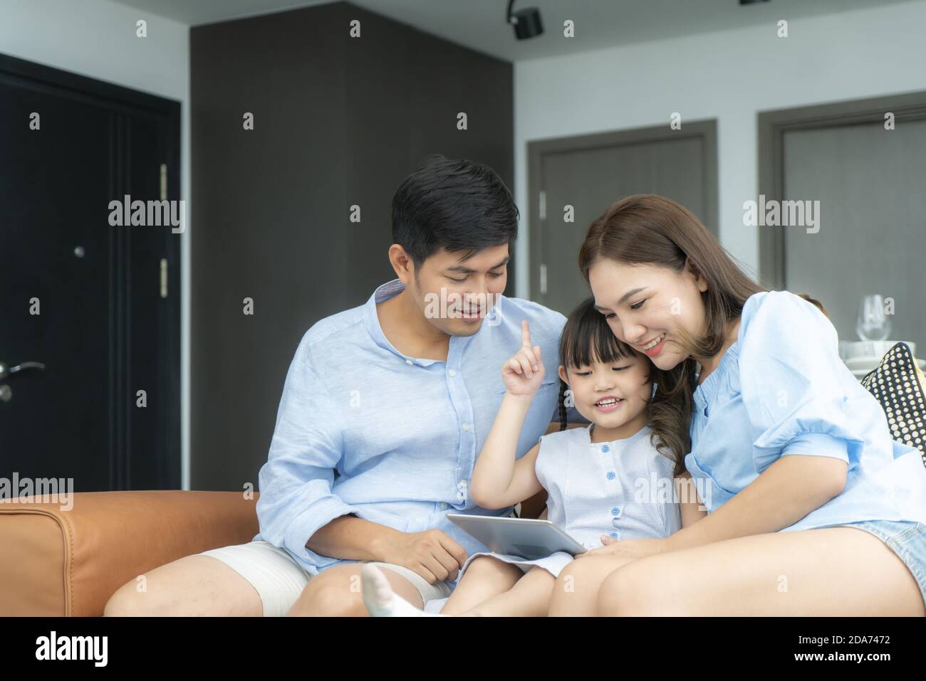 Glückliche asiatische Familie mit Vater, Mutter und Tochter sitzen auf dem Sofa und mit digitalen Tablet Blick auf den Bildschirm zusammen im Wohnzimmer zu Hause. Stockfoto
