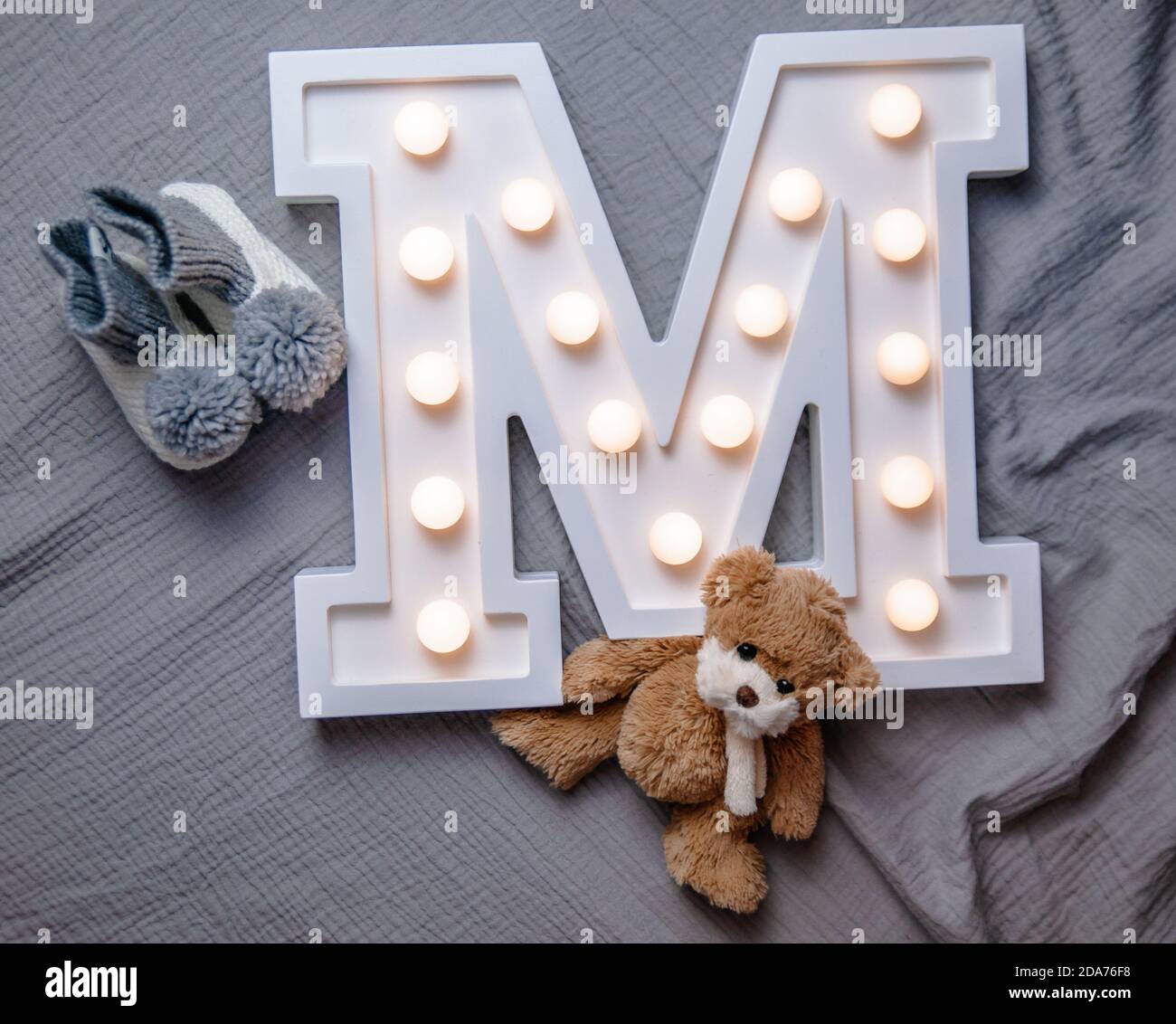 Ein weißer leichter Buchstabe M auf grauem Hintergrund mit Teddybär und Baby Pom Pom Socken. Kinderdekoration Konzept. Stockfoto