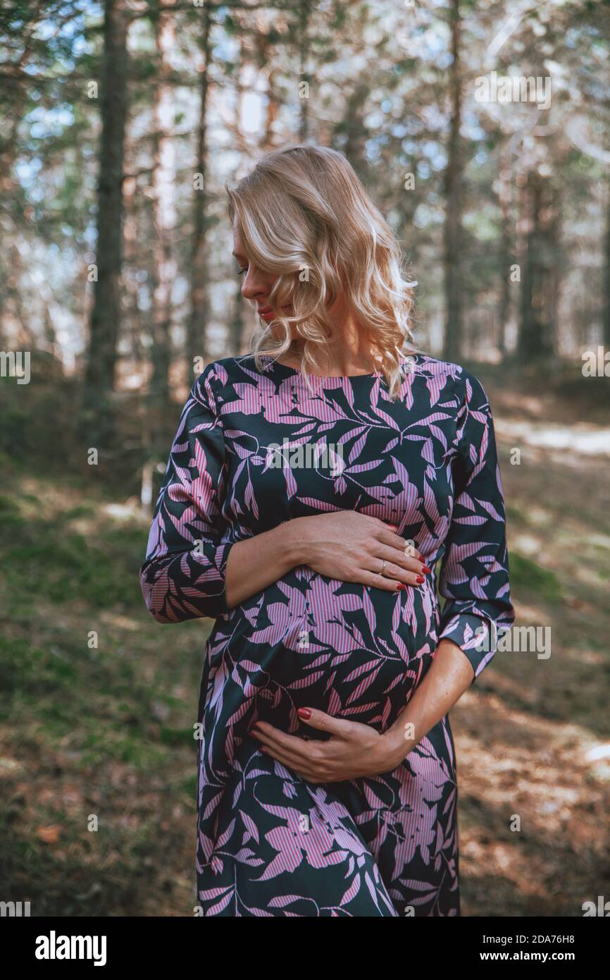 Junge schwangere Frau hält ihren Bauch in einem Wald. Herbststimmung, Sommerstimmung. Stockfoto