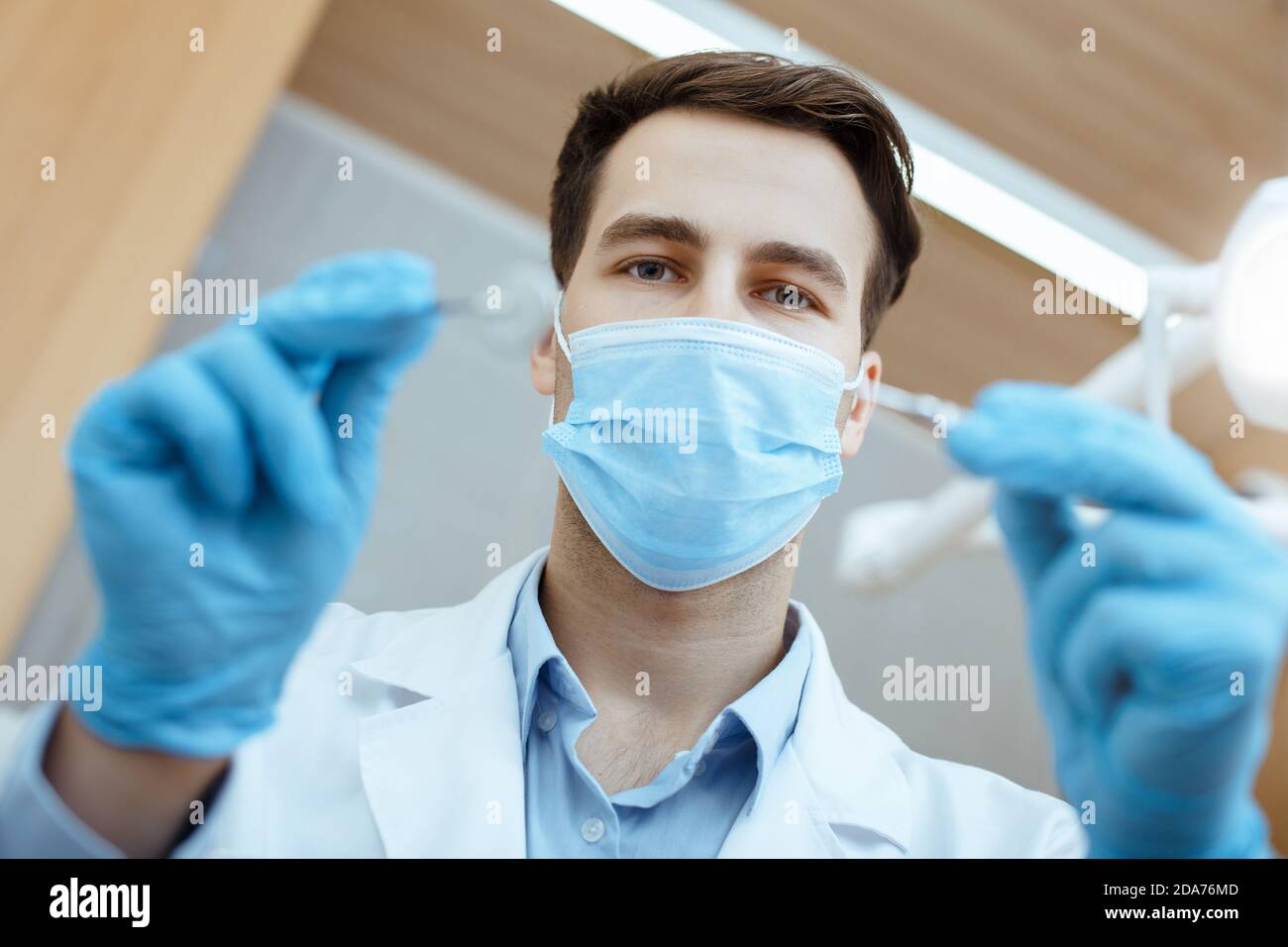 Junge attraktive Zahnarzt in weißem Mantel, Schutzmaske und Gummihandschuhe behandelt Zähne zum Patienten Stockfoto