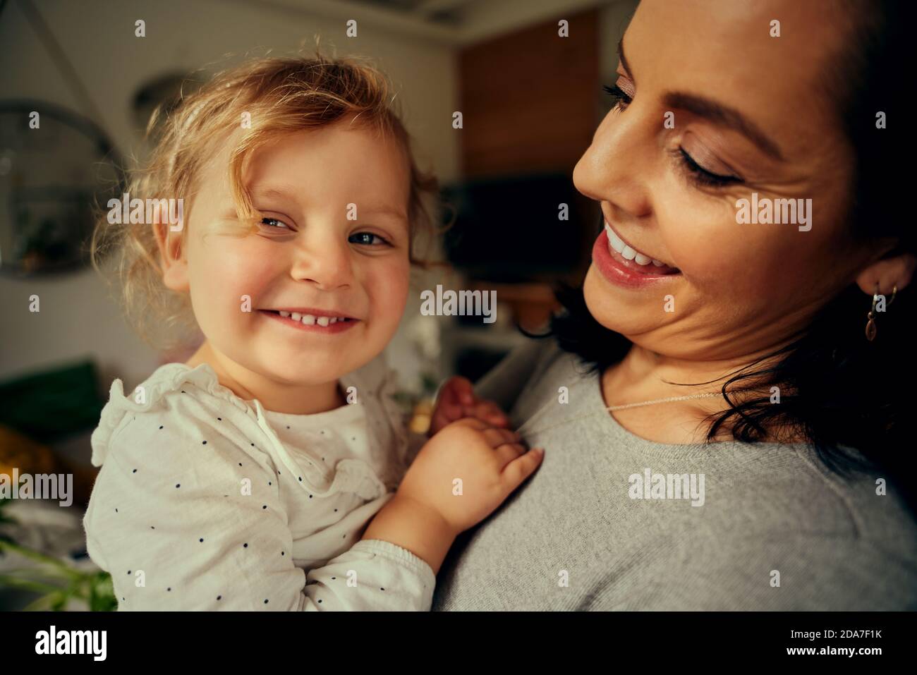 Kleine Vorschule nettes Mädchen lächelnd Blick auf Kamera auf Mutter Hände zu Hause Stockfoto