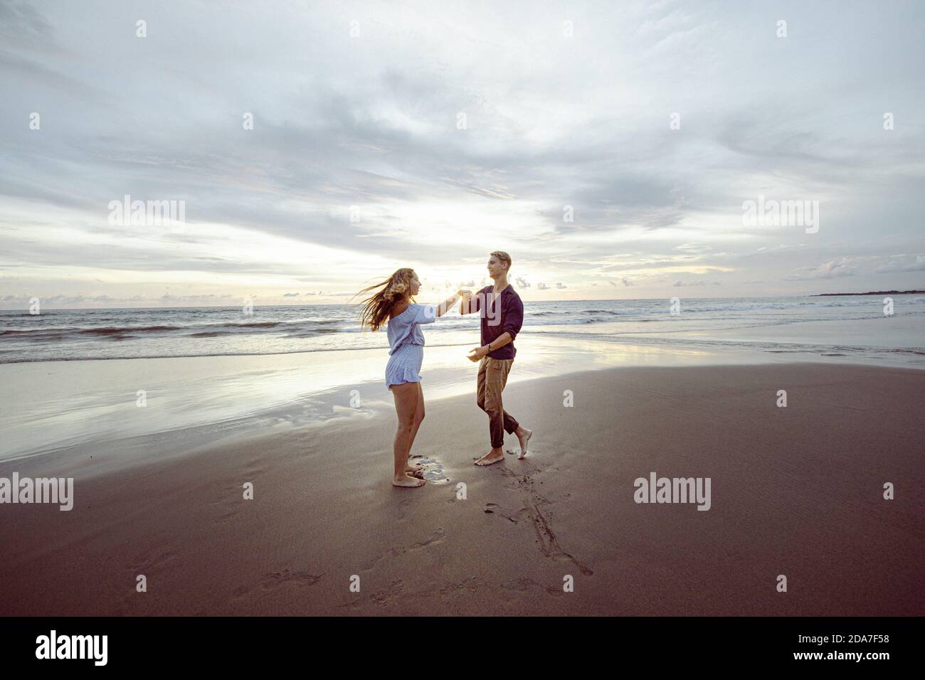 Pärchen spielen und tanzen am Strand, lachen. Sonnenuntergang an einem Strand in Bali, Indonesien Stockfoto