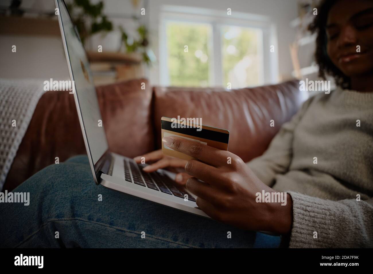 Nahaufnahme der jungen Frau Hand hält Bank Debit-Karte, während Zahlung auf Laptop zu Hause Stockfoto