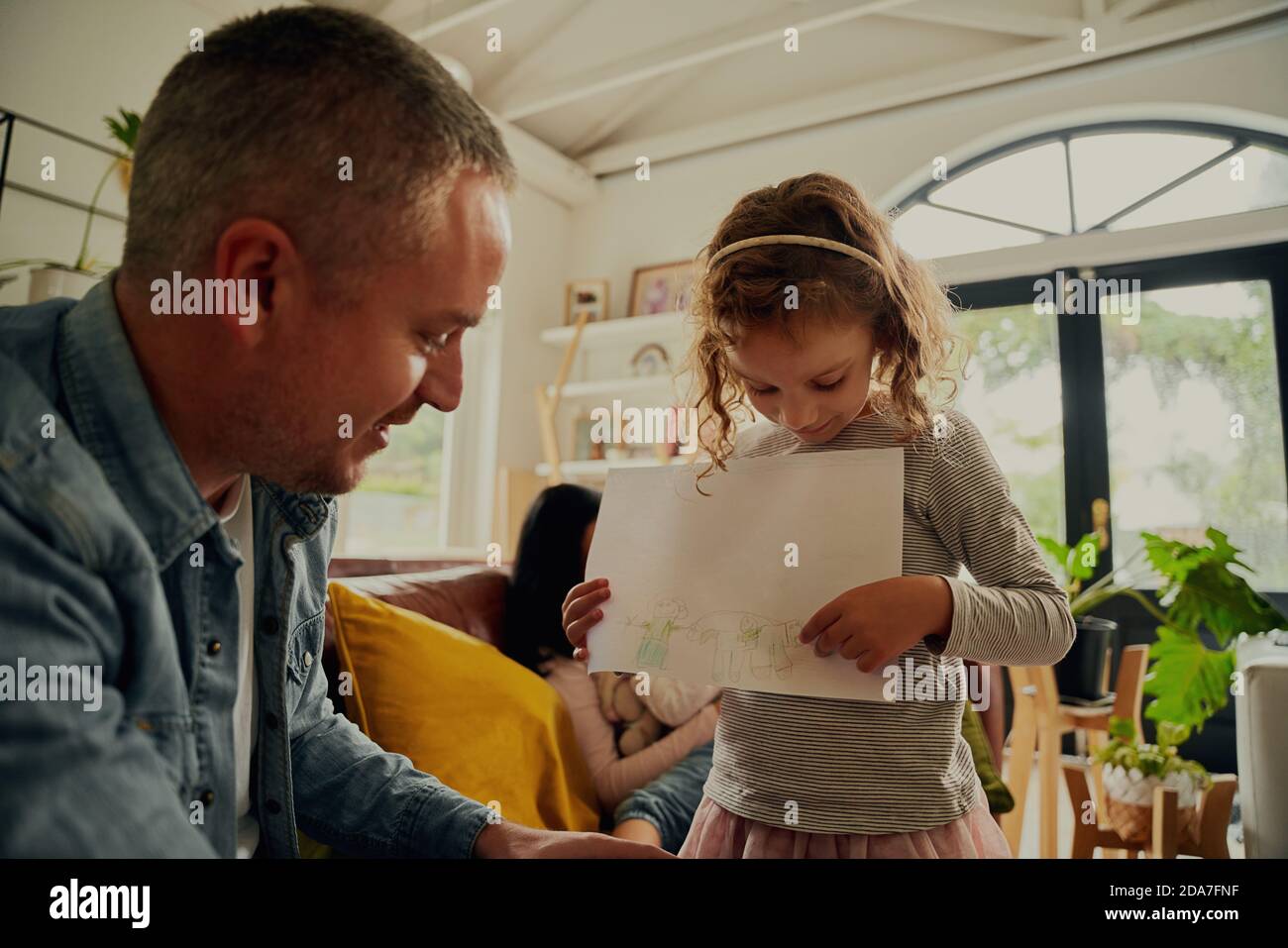 Künstlerische Tochter zeigt kreative Zeichnung auf Papier zu Vater an Zu Hause Stockfoto