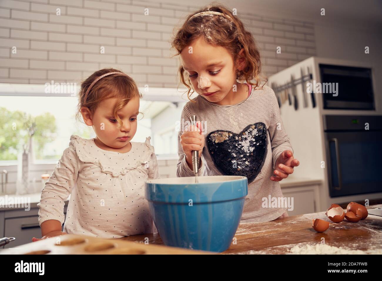 Kleine Mädchen mit Handmixer in Schüssel während der Zubereitung von Teig Mit Eiern auf Küchenablage zu Hause Stockfoto
