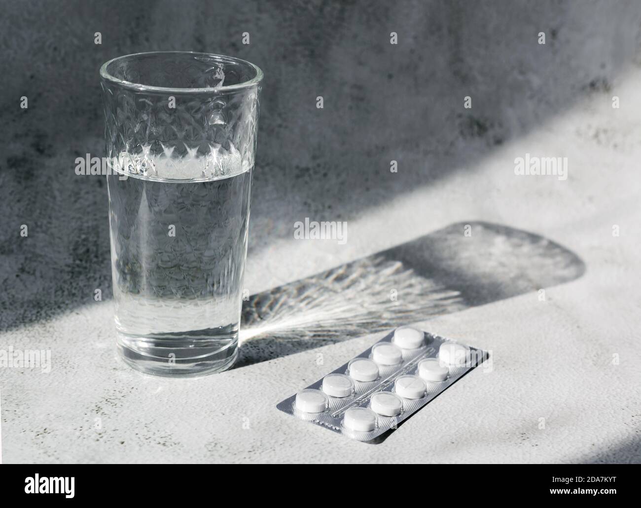 Klares Glas Wasser und Packung Pillen im Kontrast Tageslicht auf grauem Hintergrund. Kopfschmerzen oder Kater Konzept. Stockfoto