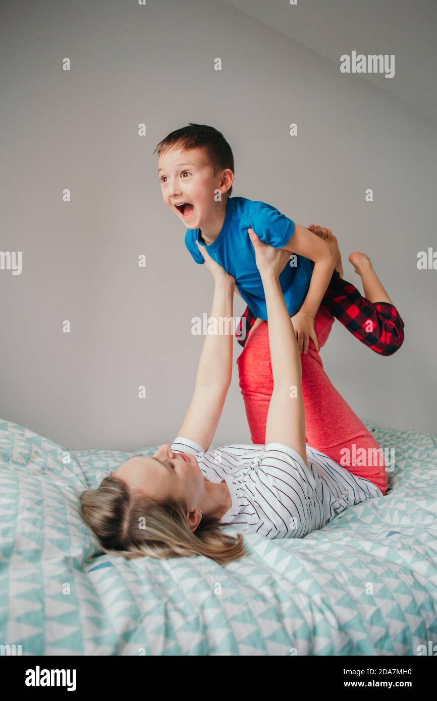 Kaukasische Mutter und Sohn spielen zu Hause im Schlafzimmer. Mutter schaukende Kinder auf den Knien der Beine. Die Familie hat Spaß zusammen. Glückliches ehrliches authentisches Kind Stockfoto