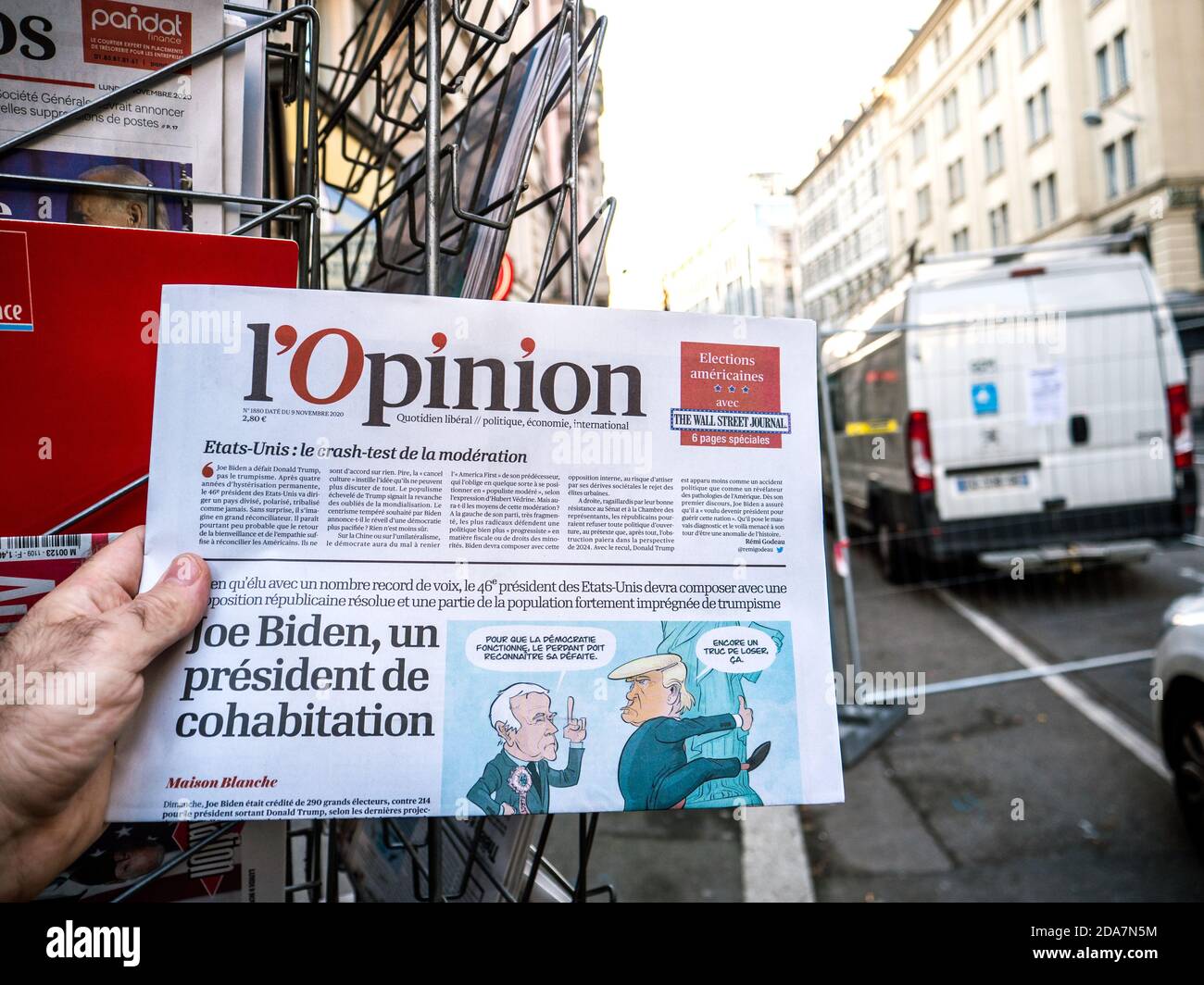 Paris, Frankreich - 9. Nov 2020: POV männliche Hand kaufen an Presse Kiosk l'Opinion Zeitung mit Karikatur von Joe Bidens projizierten US-Präsidentschaftswahlsieg gegen Amtsinhaber Donald Trump Stockfoto