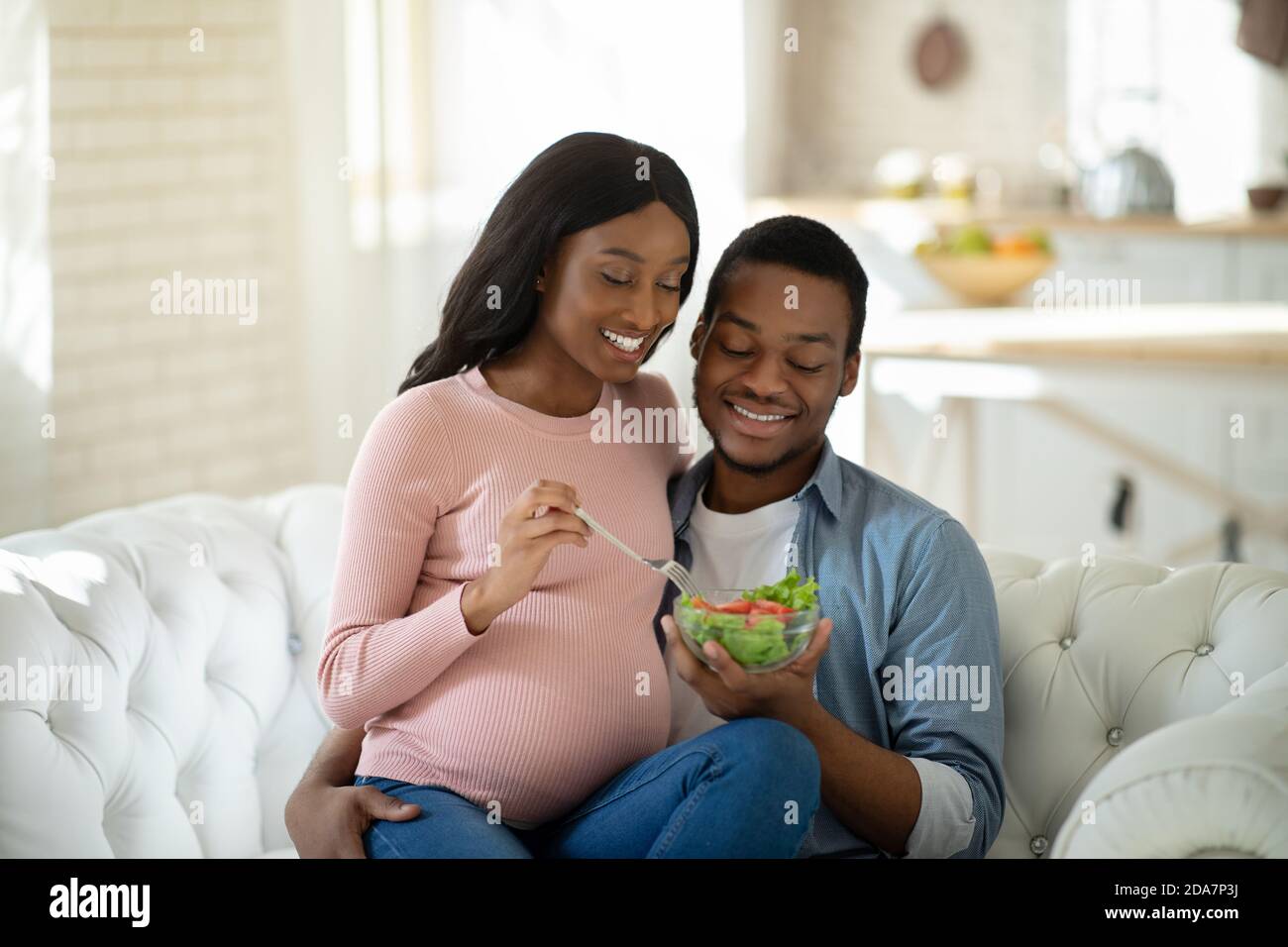 Gesunde Ernährung während der Schwangerschaft. Positiver schwarzer Ehemann und seine erwartungsvolle Frau essen frischen Gemüsesalat zu Hause Stockfoto