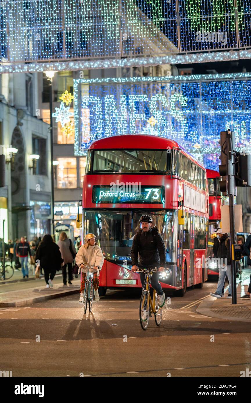 LONDON - 3. NOVEMBER 2020: Radfahrer vor einem roten London Doppeldeckerbus mit Oxford Street beleuchteten Weihnachtsdekorationen im Hintergrund Stockfoto